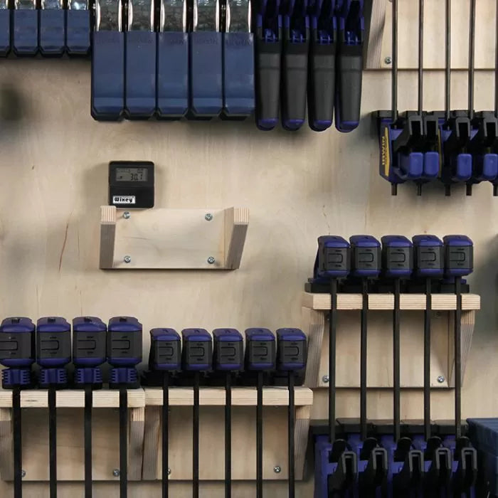 Woodworking clamps organized on a wall-mounted rack in a workshop setting