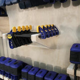Wall-mounted woodworking clamp rack holding blue and yellow bar clamps in workshop