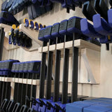 Woodworking bar clamps organized on a wall-mounted clamp rack in a workshop