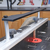 Router table setup with fence, router bit, dust hose, and measuring guide in a workshop