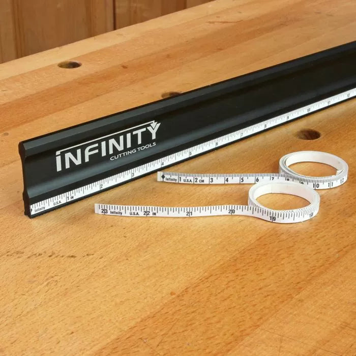 Black woodworking ruler with printed branding and a flexible tape measure on a wooden table.