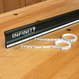 Black woodworking ruler with printed branding and a flexible tape measure on a wooden table.