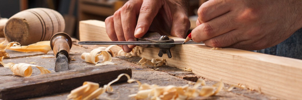 Woodworker marking wood with precision tool amid wood shavings on a workbench.