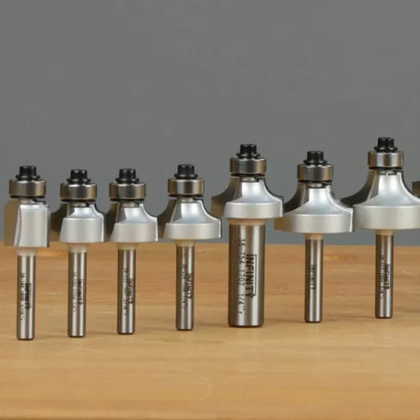 Assorted roundover router bits with bearings arranged on a wooden surface, woodworking tools