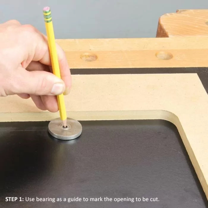 Hand using bearing and pencil to mark cut line on router table insert for woodworking.