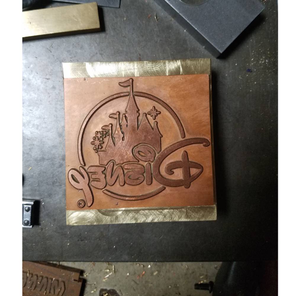 Custom engraved branding iron with castle and stylized text on a metal plate, workshop table