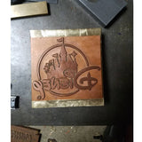 Custom engraved branding iron with castle and stylized text on a metal plate, workshop table