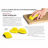Yellow sanding pads for woodworking, one in use on a wood block, ergonomic design shown.