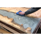 Hand polishing a live edge epoxy resin river table on a woodworking bench
