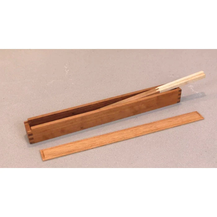 Wooden dovetail box with removable lid, holding thin wood strips on a light surface