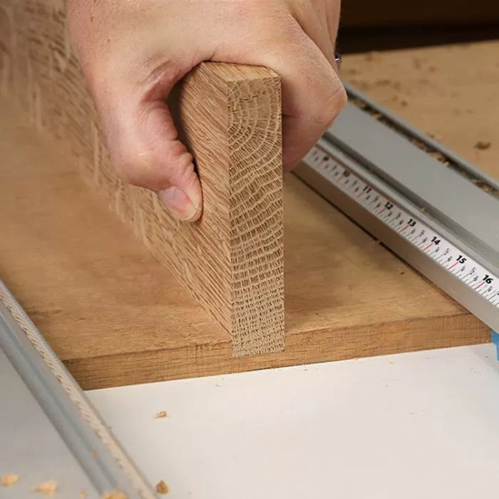 Hand holding cut oak board on woodworking router table next to a measuring guide