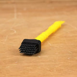 Yellow detail cleaning brush with black bristles on a wooden workbench