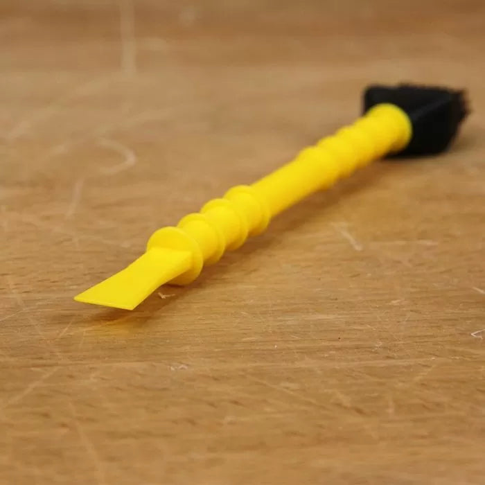 Yellow plastic woodworking bench brush and scraper on a wooden workbench