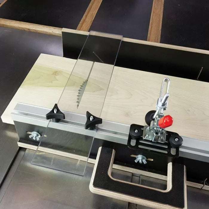 Table saw crosscut sled with stop block, hold-down clamp, and clear blade guard for woodworking.