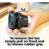 Hands pulling apart Uni-Vac dust collection adapter with rubber grip on woodworking table.