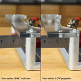 Close-up of adjustable router table visor extension showing two different projection settings with ruler measurements on a woodworking bench.