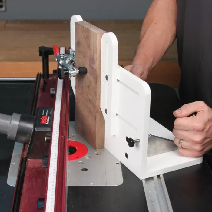 Woodworker using a router table with a vertical sled to guide a wood board for precise cuts